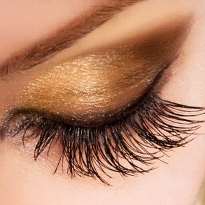 Woman eye with extremely long eyelashes and golden makeup
